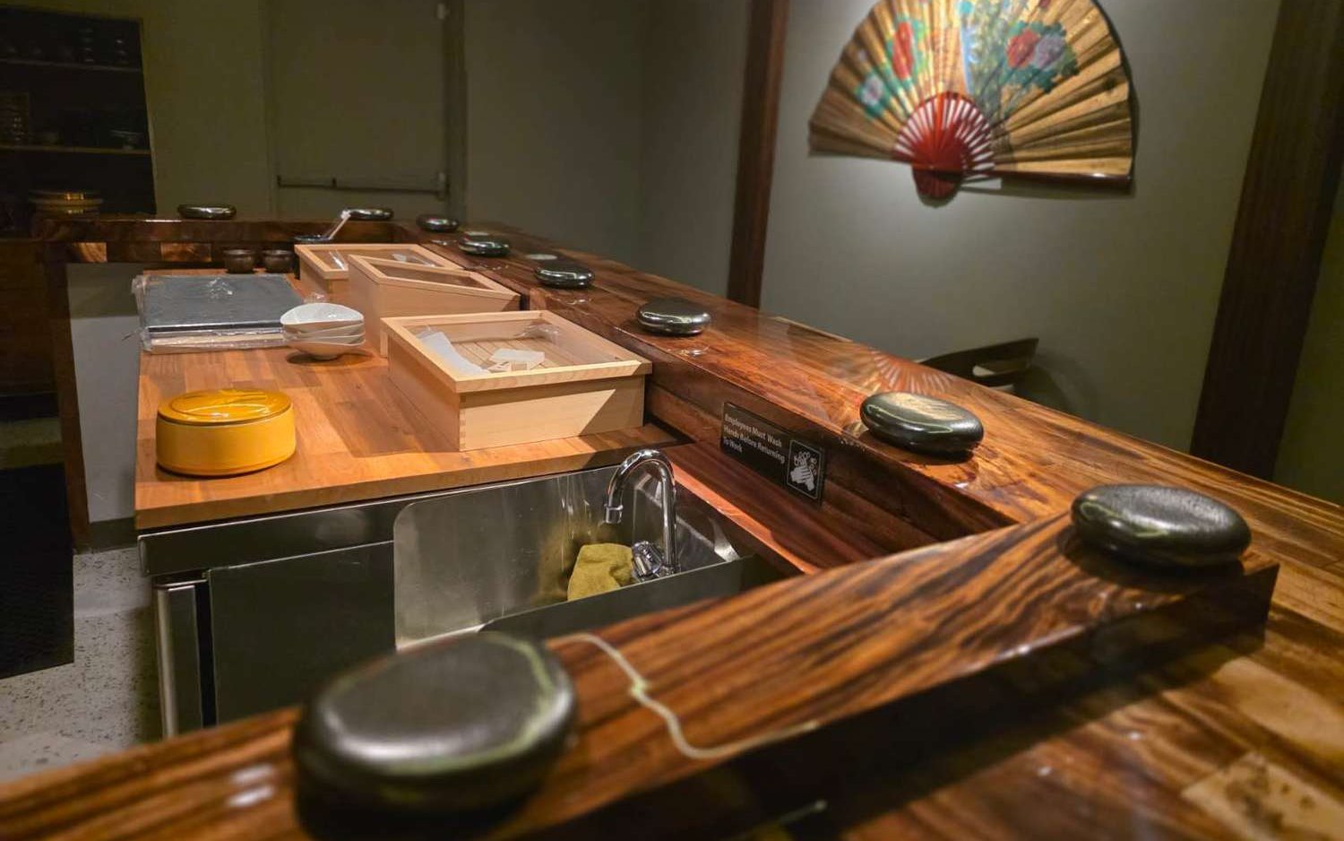 KoBu's live-edge wooden sushi counter with stone rests and a painted Japanese fan on the wall