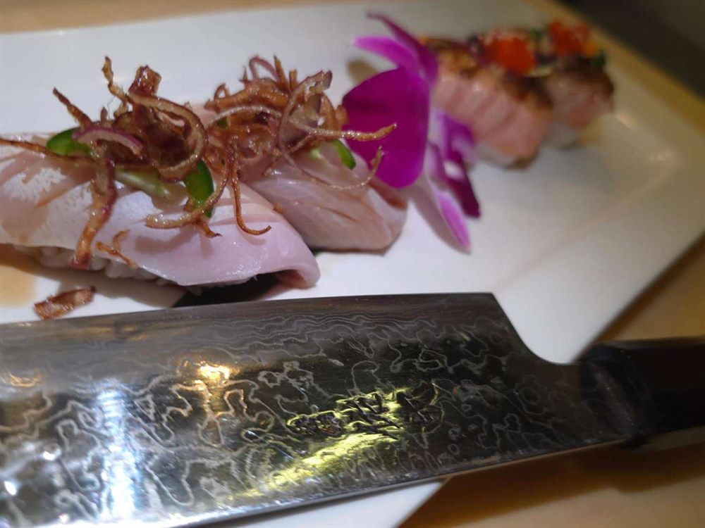 Yellowtail nigiri beside a damascus-steel knife