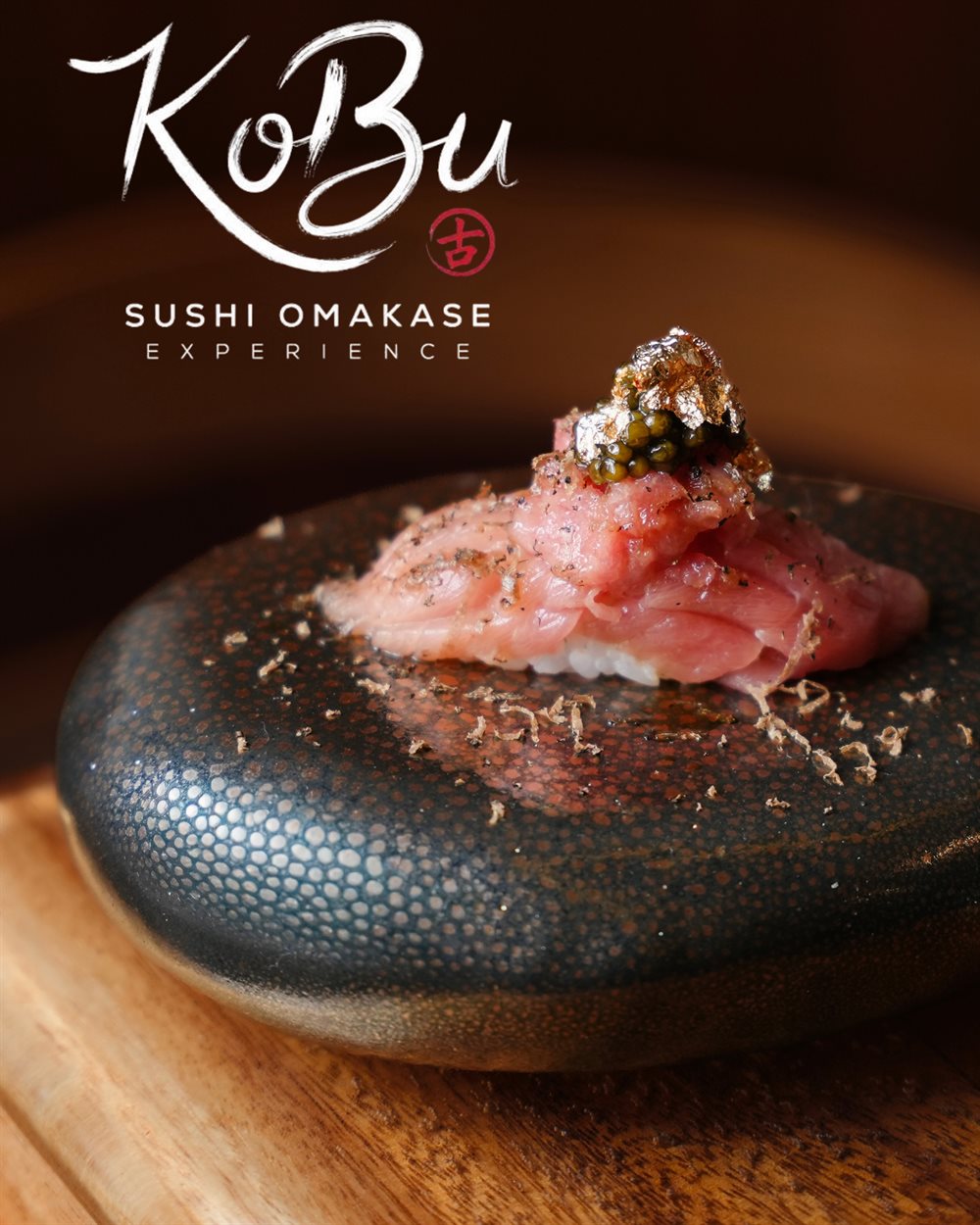 Toro nigiri topped with caviar and gold leaf, dusted with shaved truffle on a dark stone plate